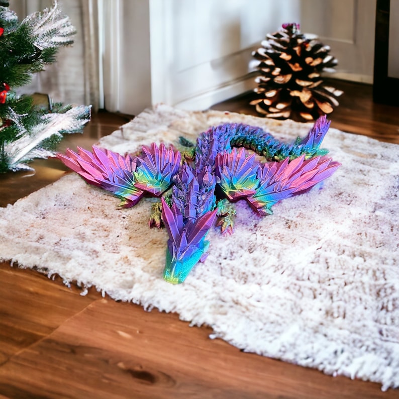 May include: A colorful iridescent dragon figurine with wings spread out, made of a crystal-like material. The dragon is lying on a white fluffy rug.