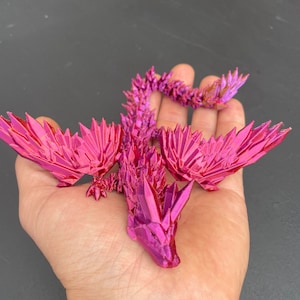 May include: A pink origami dragon with a spiky, crystalline appearance. The dragon is posed with its wings spread and its tail curled.