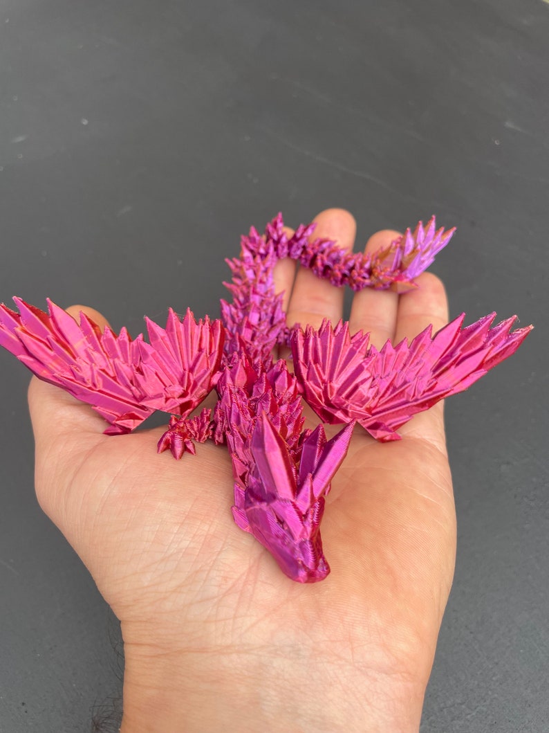 May include: A pink origami dragon with a spiky, crystalline appearance. The dragon is posed with its wings spread and its tail curled.