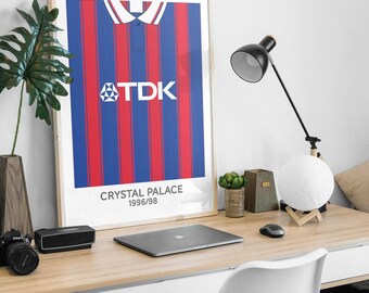 May include: A framed vertical poster featuring a graphic illustration of a Crystal Palace 1996/98 football shirt with red and blue vertical stripes, a white collar, and the TDK logo printed in white across the centre of the chest area.