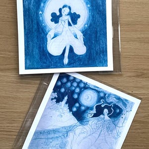 May include: Two blue-toned art prints featuring illustrations of women. One shows a woman in a flowing gown against a moon and stars. The other depicts a woman with long hair, a spiderweb-like dress, and a night sky background.