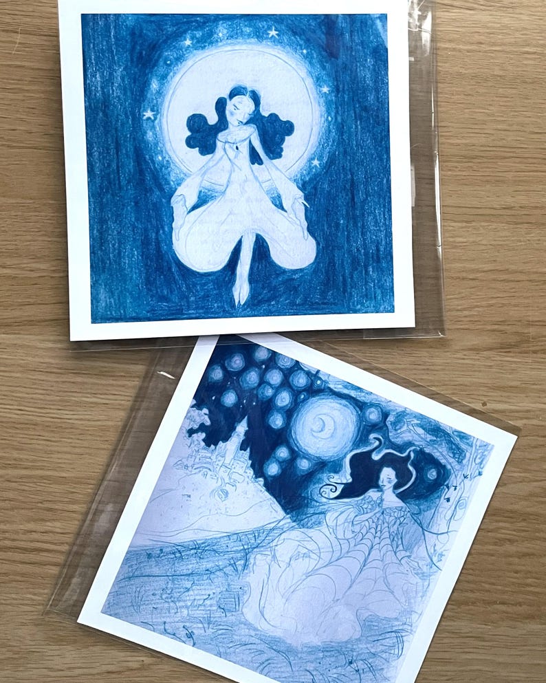 May include: Two blue-toned art prints featuring illustrations of women. One shows a woman in a flowing gown against a moon and stars. The other depicts a woman with long hair, a spiderweb-like dress, and a night sky background.