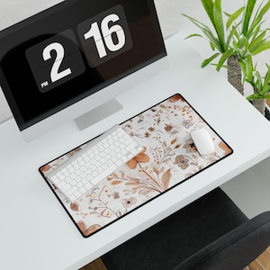 May include: A white desk mat with a floral pattern in shades of brown and beige. A white keyboard and mouse are on the mat.