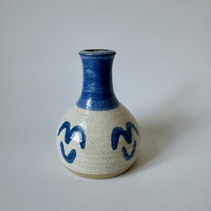 Może przedstawiać: Mały, ręcznie robiony ceramiczny wazon o zaokrąglonym korpusie i wąskiej szyi. Górna część i szyja są w kolorze granatowym, kontrastującym z kremowym korpusem. Dwa niebieskie abstrakcyjne wzory są namalowane na korpusie. Odpowiedni do małych kwiatów.