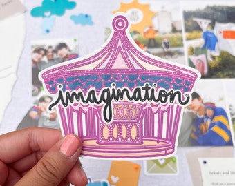 May include: A pink and blue sticker with a carousel design and the word "imagination" written in black cursive. The sticker is on a white background.