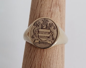 May include: A gold signet ring with an oval-shaped crest featuring a coat of arms and the name "Rivers" engraved below.
