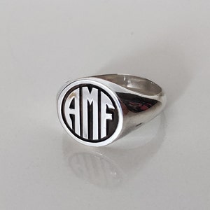 May include: A silver signet ring with a black oval-shaped setting featuring the initials "AMF" in white.