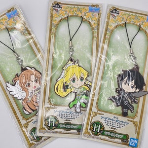 May include: Three Sword Art Online: Alicization - War of Underworld rubber keychains featuring the characters Eugeo, Alice, and Kirito. The keychains are packaged in clear plastic bags with a green and gold background.