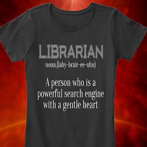 Puede incluir: Una camiseta gris oscuro con el texto "LIBRARIAN noun.(lahy-brair-ee-uhn) A person who is a powerful search engine with a gentle heart" impreso en blanco.