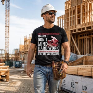 Può includere: Una t-shirt nera a maniche corte con la grafica di un operaio edile e il testo: I'M A CONSTRUCTION WORKER BECAUSE I DON'T MIND HARD WORK. IF I WANTED TO DO SOMETHING EASY I'D CALL YOUR MOM. La maglietta è indossata con un paio di jeans blu.