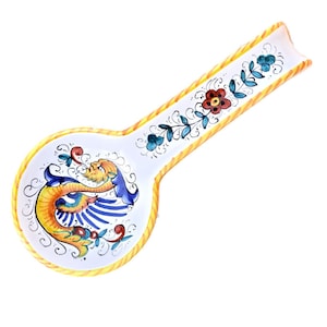 May include: A white ceramic spoon rest with a yellow, blue and red floral design and a yellow dragon with blue wings.