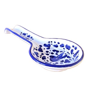 Può includere: Un poggia-cucchiaio in ceramica bianca con un design floreale blu e bianco. Il poggia-cucchiaio ha un manico lungo e una ciotola arrotondata.