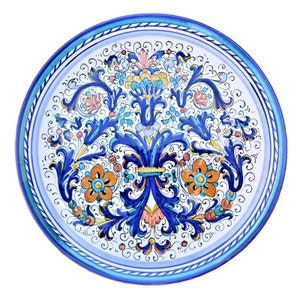 Peut inclure: Une assiette en céramique blanche avec une bordure bleue et blanche et un motif floral coloré au centre. Le motif présente des fleurs et des feuilles bleues, orange, jaunes et roses.