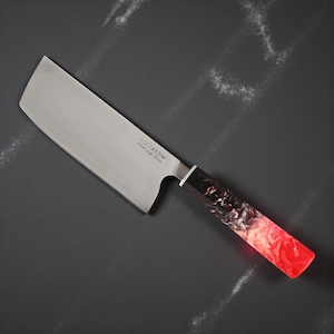 May include: A stainless steel chef's knife with a rectangular blade and a colourful handle. The handle has a black, white, and red marbled design. The knife is angled on a dark grey surface.
