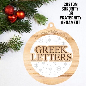 Può includere: Un ornamento rotondo in legno con sfondo bianco e fiocchi di neve. L'ornamento dice "ORGANIZATION NAME" in alto e "GREEK LETTERS" al centro.