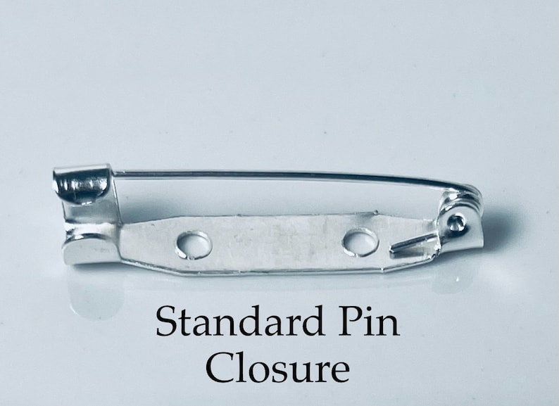 May include: A silver standard pin closure for attaching jewelry or other items to clothing. The pin has a spring-loaded mechanism and a safety catch.