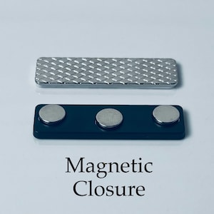May include: A silver magnetic closure with a textured surface. The closure has three black magnets. The text "Magnetic Closure" is printed below the closure.