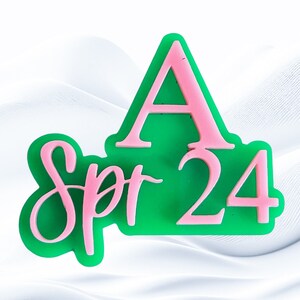 May include: A green and pink acrylic sign with the text "Spr 24" and a large pink letter "A" above the text.