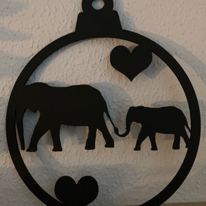 May include: Black wooden ornament shaped like a Christmas tree bauble with two elephants holding trunks together inside. There are two black hearts on the ornament.