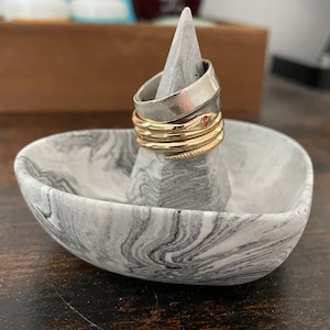May include: A set of four rings stacked on a grey marble ring holder. The rings are made of silver, gold, and a snake design with red eyes.