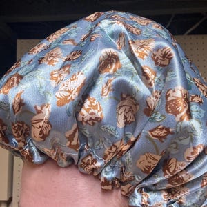K&ouml;nnte beinhalten: Eine blaue Satin-Schlafhaube mit einem Blumenmuster mit braunen Rosen. Die Haube ist oben gerafft und hat ein wei&szlig;es Gummiband.