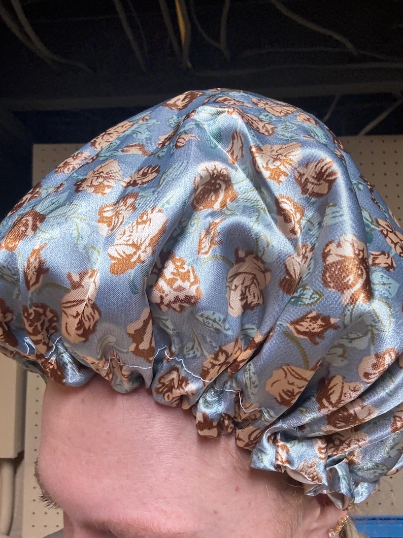 K&ouml;nnte beinhalten: Eine blaue Satin-Schlafhaube mit einem Blumenmuster mit braunen Rosen. Die Haube ist oben gerafft und hat ein wei&szlig;es Gummiband.