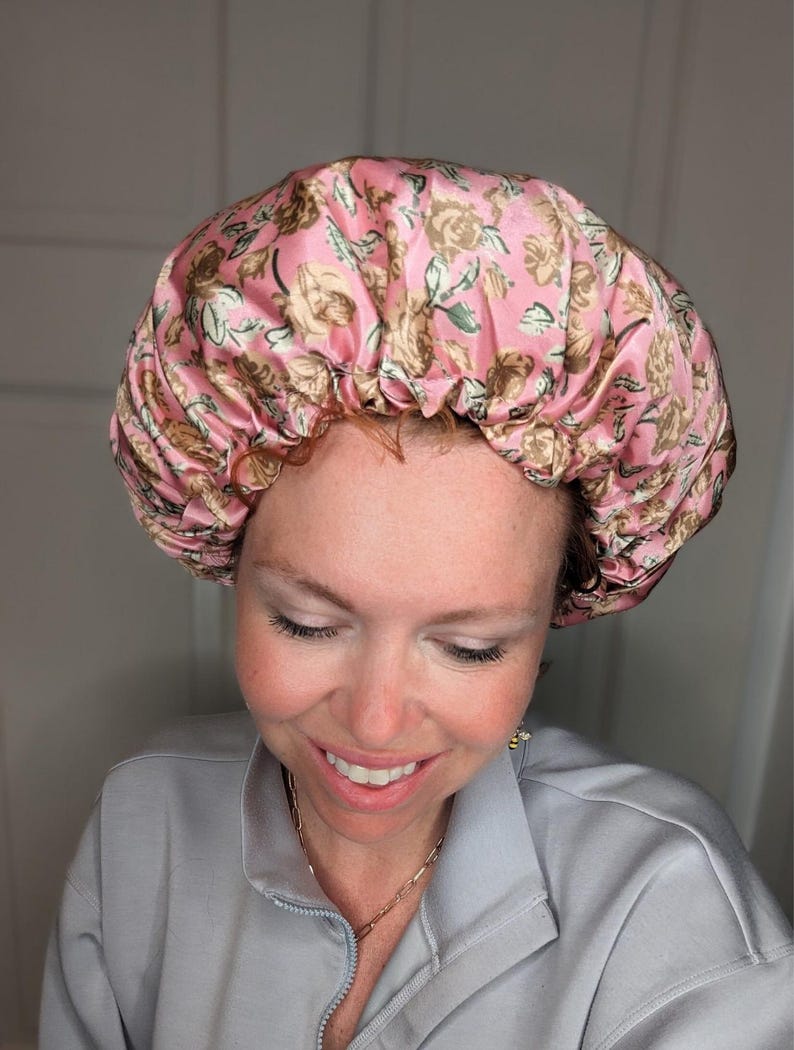 K&ouml;nnte beinhalten: Eine rosa Satin-Schlafhaube mit Blumenmuster. Die Haube ist oben gerafft und hat einen Kordelzug.