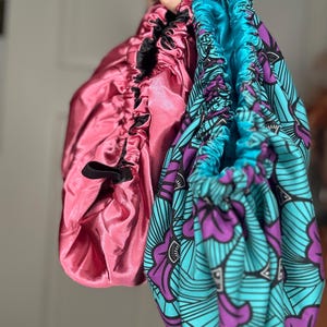 K&ouml;nnte beinhalten: Zwei Satin-Haarb&auml;nder, eines rosa und eines blau mit einem violetten und schwarzen Blumenmuster.