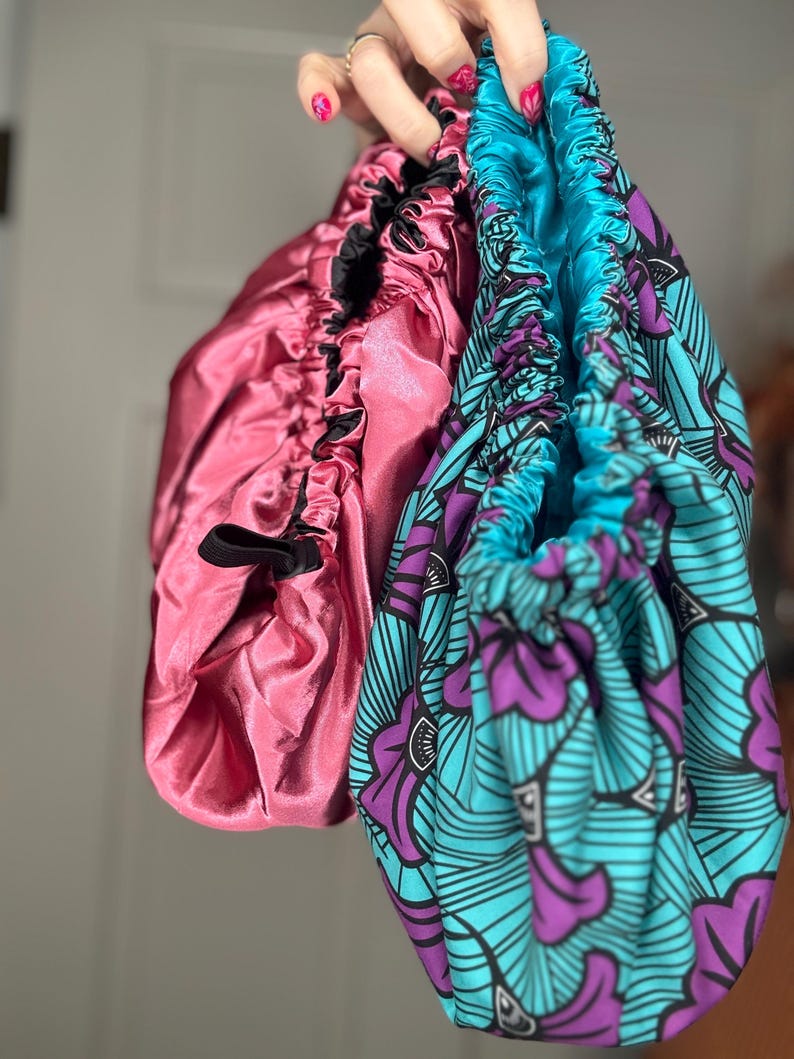 K&ouml;nnte beinhalten: Zwei Satin-Haarb&auml;nder, eines rosa und eines blau mit einem violetten und schwarzen Blumenmuster.