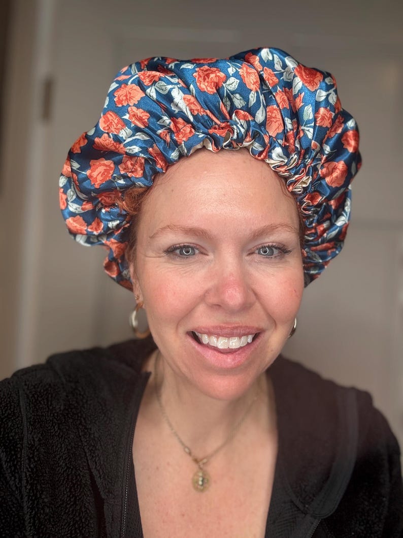 K&ouml;nnte beinhalten: Eine Frau tr&auml;gt eine blaue und orangefarbene Satin-Schlafhaube mit Blumenmuster. Die Haube ist oben gerafft und hat ein wei&szlig;es Gummiband.