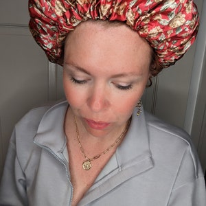 K&ouml;nnte beinhalten: Eine Frau tr&auml;gt eine rote und wei&szlig;e Satin-Schlafhaube mit Blumenmuster. Sie tr&auml;gt einen hellblauen Pullover mit Rei&szlig;verschluss.