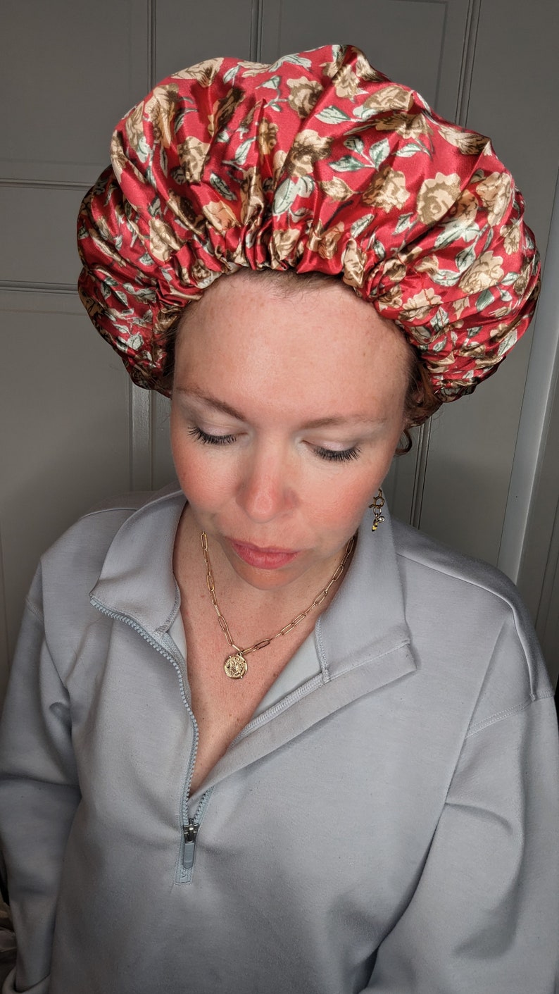K&ouml;nnte beinhalten: Eine Frau tr&auml;gt eine rote und wei&szlig;e Satin-Schlafhaube mit Blumenmuster. Sie tr&auml;gt einen hellblauen Pullover mit Rei&szlig;verschluss.