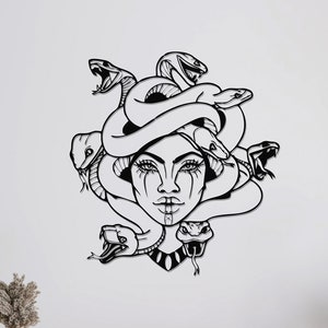 May include: Black and white line art wall decor of a woman's face with snakes for hair. The woman has a dramatic expression with dark eyes and a single tear on her cheek. The snakes are intertwined around her head and neck.