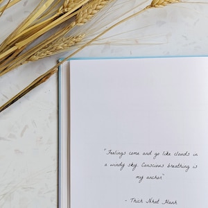 May include: A white notebook with a quote by Thich Nhat Hanh written in black ink. The quote reads "Feelings come and go like clouds in a windy sky. Conscious breathing is my anchor."