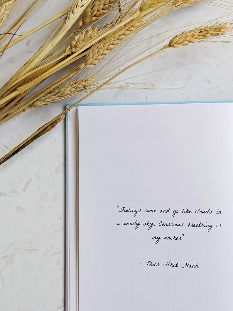 May include: A white notebook with a quote by Thich Nhat Hanh written in black ink. The quote reads "Feelings come and go like clouds in a windy sky. Conscious breathing is my anchor."