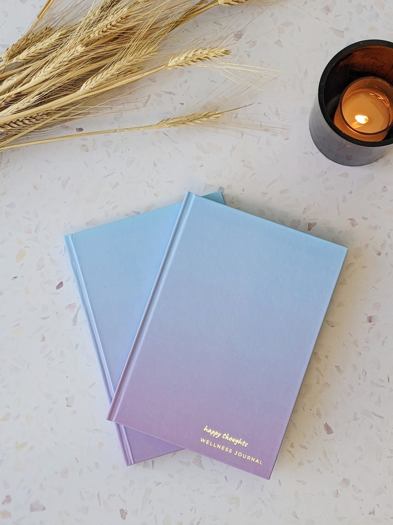 May include: Two blue and purple gradient journals with the text "happy thoughts WELLNESS JOURNAL" on the front.