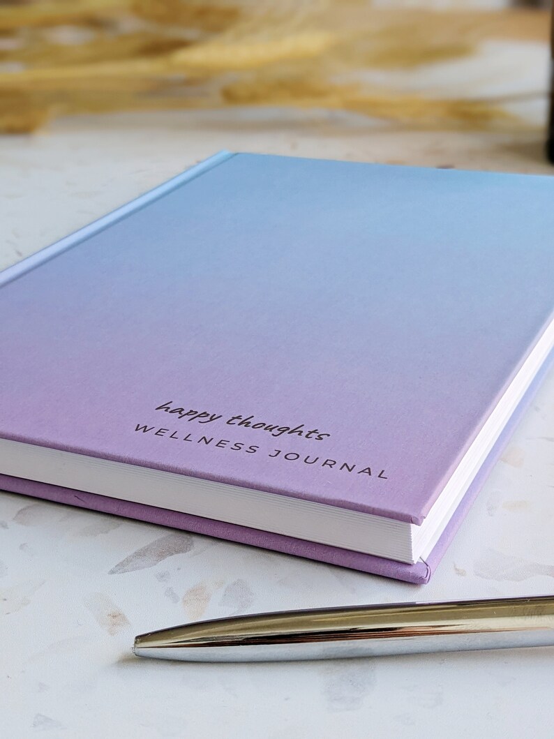 May include: A purple and blue ombre journal with the text "happy thoughts WELLNESS JOURNAL" on the cover.