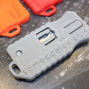 May include: A grey, textured, keychain-sized multi-tool with a small blade and the text "spremeca.com" printed on the side.