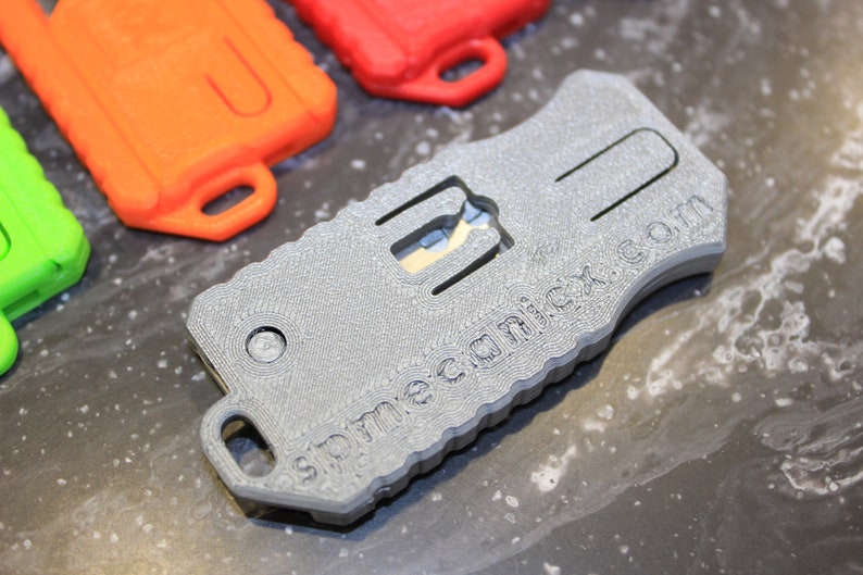 May include: A grey, textured, keychain-sized multi-tool with a small blade and the text "spremeca.com" printed on the side.