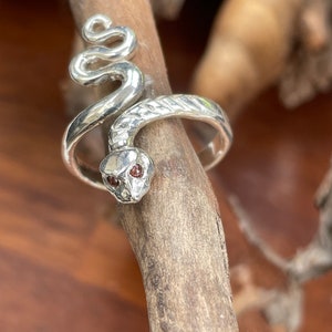 May include: A silver snake ring with red gemstone eyes. The snake is coiled and the ring is textured.