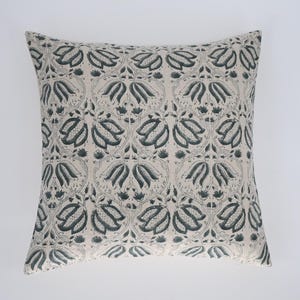May include: Square decorative pillow with a repeating floral pattern in shades of teal and gray on a cream background. The pillow has a symmetrical design, suitable for a living room or bedroom.