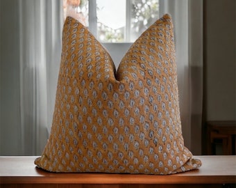 Può includere: Un cuscino da lancio giallo e blu con un design geometrico sottile. Il cuscino è su una superficie di legno.