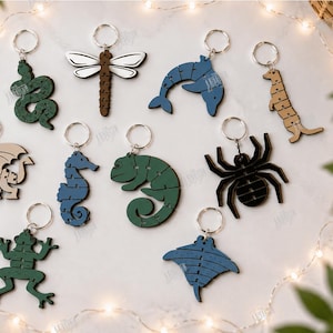 May include: A collection of ten laser-cut animal keychains featuring a snake, dragonfly, dolphin, meerkat, dragon, seahorse, chameleon, spider, frog, and stingray. Each keychain includes a metal ring and displays segmented puzzle-like lines.