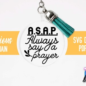 Pu&ograve; includere: Un portachiavi rotondo bianco con un fiocco turchese. Il portachiavi ha il testo nero che recita "A.S.A.P. Always say a prayer".
