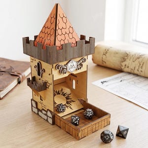 Könnte beinhalten: Ein lasergeschnittener Würfelturm aus Holz mit beigefarbener Hauptstruktur, dunkelbraunem Zinnenabschluss und strukturiertem orangefarbenem Dach. Der Turm enthält eine Sonnengravur auf dem Boden, ein W20-Emblem und mehrere schwarze Würfel.