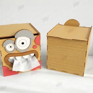 May include: Two wooden tissue box holders. One is designed with a cartoon monster face, featuring large eyes, a mouth with teeth, and red accents. The other is a plain wooden box with a lid. The text on the right says "CUT READY FILE" and "MATERIAL WIDTH: 3MM".