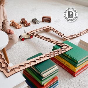 May include: A wooden marble run with a zigzag design, alongside small wooden toy cars and a bus. The image also shows a stack of books and the text "CUT READY FILE DIGITAL DOWNLOAD".