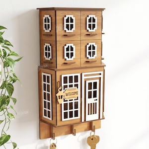 May include: A wooden wall-mounted key holder shaped like a two-story house with white window frames, a door, and a sign reading WELCOME. It features four small drawers on the top level and three hooks at the bottom for keys. Material width: 3mm.