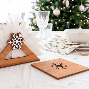 May include: A triangular wooden napkin holder featuring a white snowflake cutout and a matching square wooden coaster with a snowflake cutout. The set is crafted from 3mm thick material, designed for holiday table settings with white napkins.