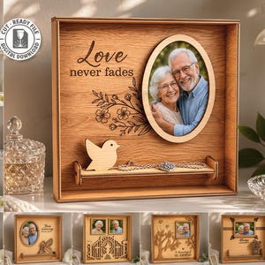 Könnte beinhalten: Ein quadratischer Holzrahmen als Schattenbox mit ovalem Fotoeinsatz, einer lasergeschnittenen Vogelsilhouette und einem kleinen Regal. Das Holz ist mit dem Text Love never fades und einem Blumenmotiv graviert. Ausgelegt für 3mm Materialstärke.